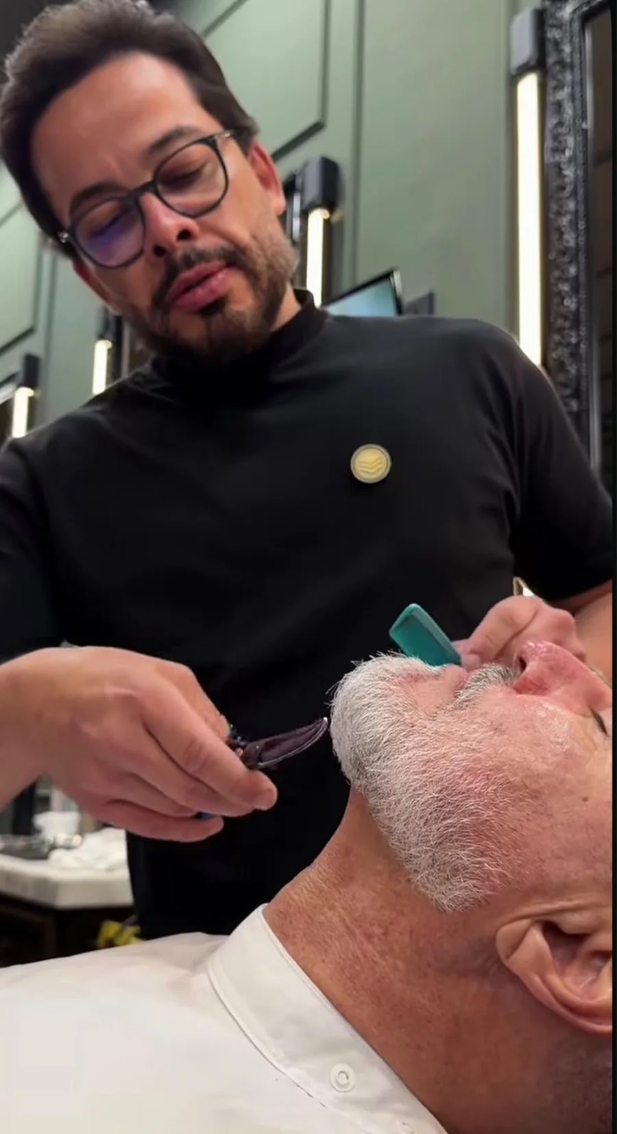 Juarez finalizando a barba de um cliente relaxado na cadeira